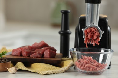 Photo of Electric meat grinder with beef mince on white table against blurred background, selective focus. Space for text