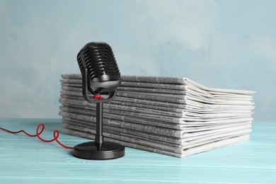 Newspapers and vintage microphone on light blue wooden table. Journalist's work