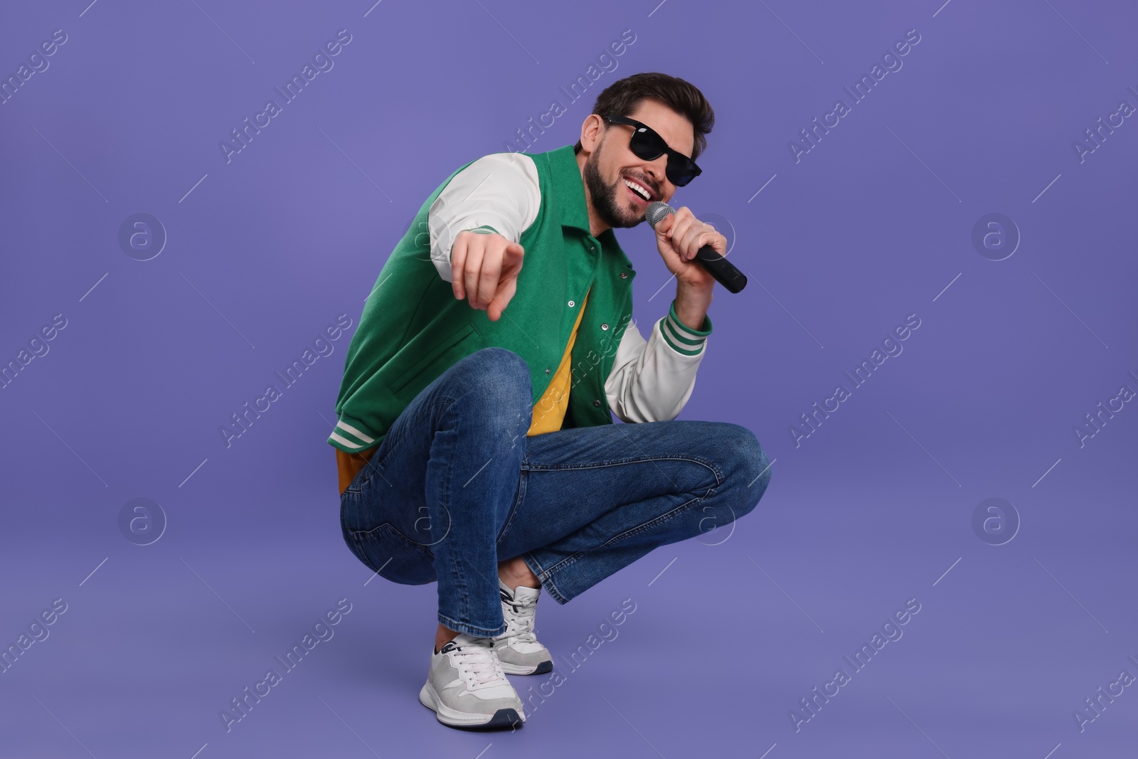 Photo of |Handsome man with sunglasses and microphone singing on purple background