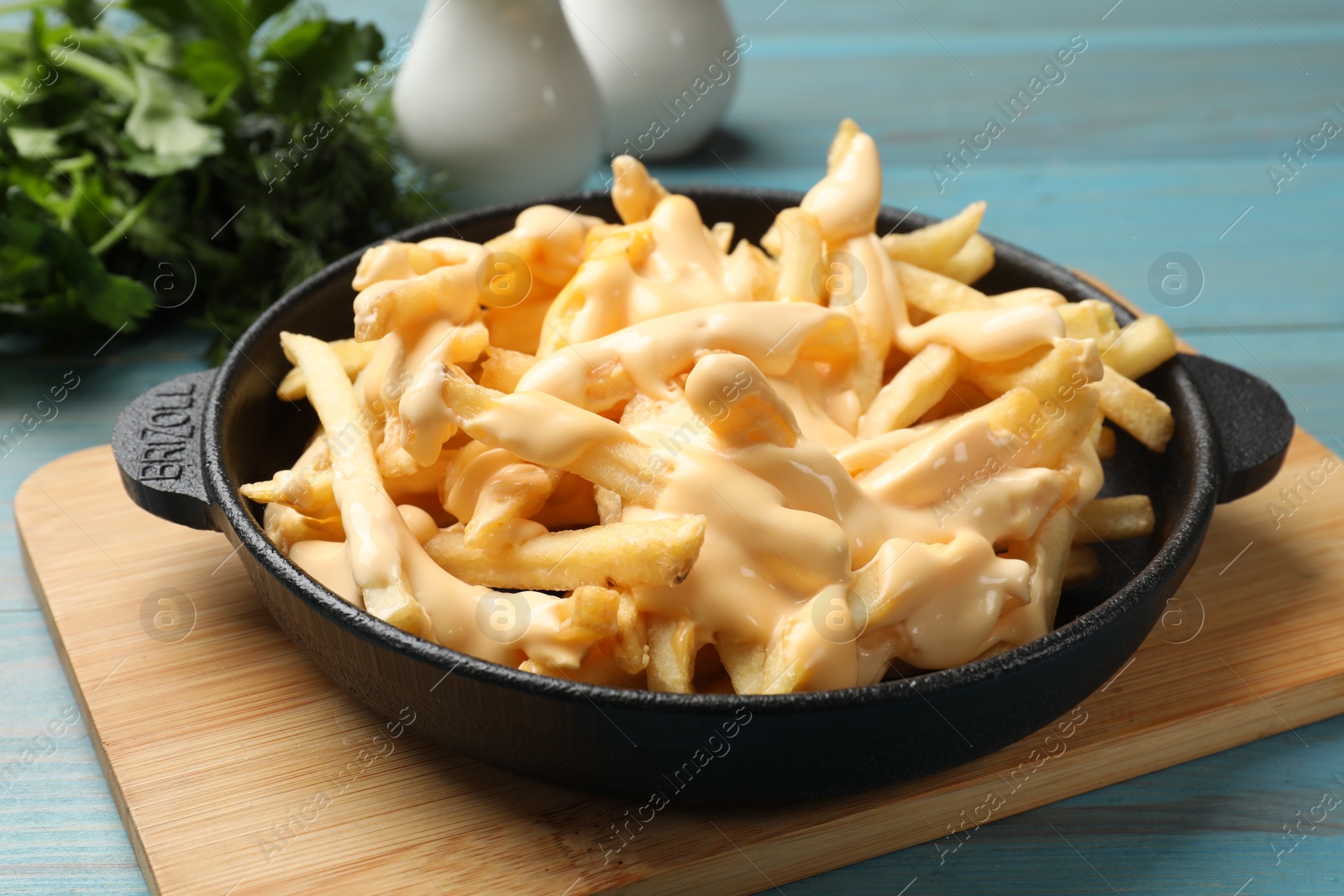 Photo of Delicious french fries with cheese sauce in bowl on light blue wooden table, closeup