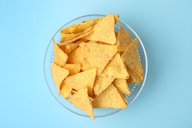 Glass bowl of tasty Mexican nachos chips on light blue background, top view