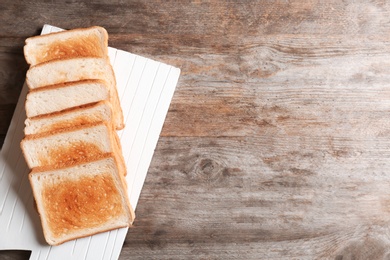 Board with toasted bread on wooden background, top view