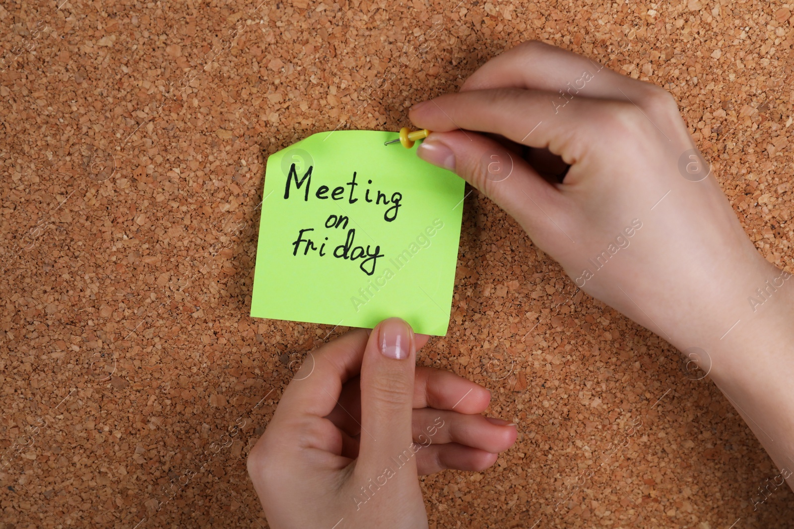 Photo of Woman pinning paper note with phrase Meeting On Friday to cork board, closeup