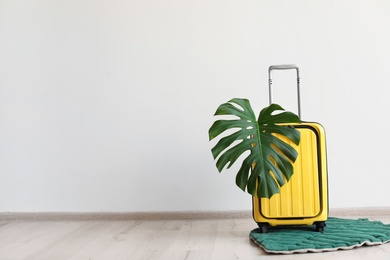 Photo of Bright yellow suitcase with tropical leaf indoors