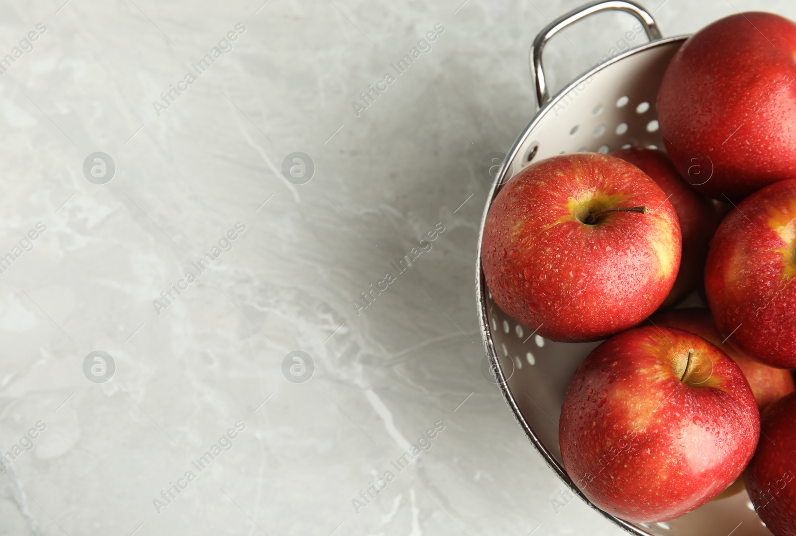 Photo of Colander with ripe juicy red apples on grey background, top view. Space for text