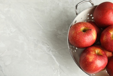 Photo of Colander with ripe juicy red apples on grey background, top view. Space for text