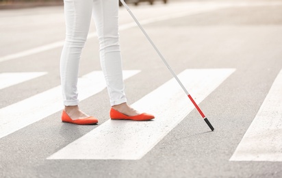 Blind person with long cane crossing road, closeup