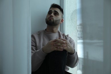 Photo of Sad man sitting near window at home