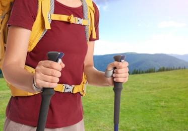 Woman with backpack and trekking poles in mountains on sunny day, closeup