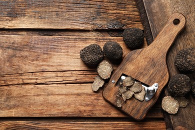 Photo of Shaver with whole and sliced black truffles on wooden table, flat lay. Space for text