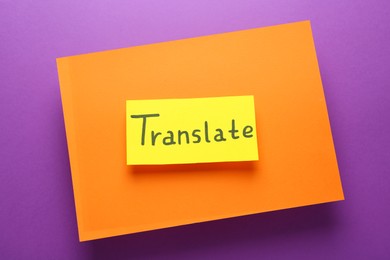 Photo of Card with word Translate and sheet of orange paper on violet background, top view