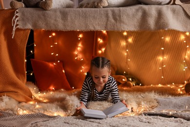 Girl reading book in decorated play tent at home