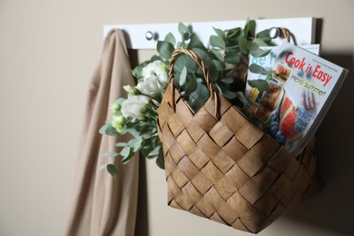Photo of Stylish straw bag with beautiful bouquet hanging on grey wall