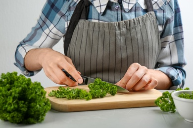 Photo of Woman cutting curly parsley at light grey table, closeup