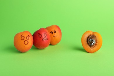Photo of Apricots with drawn faces on green background. Exhibitionist concept
