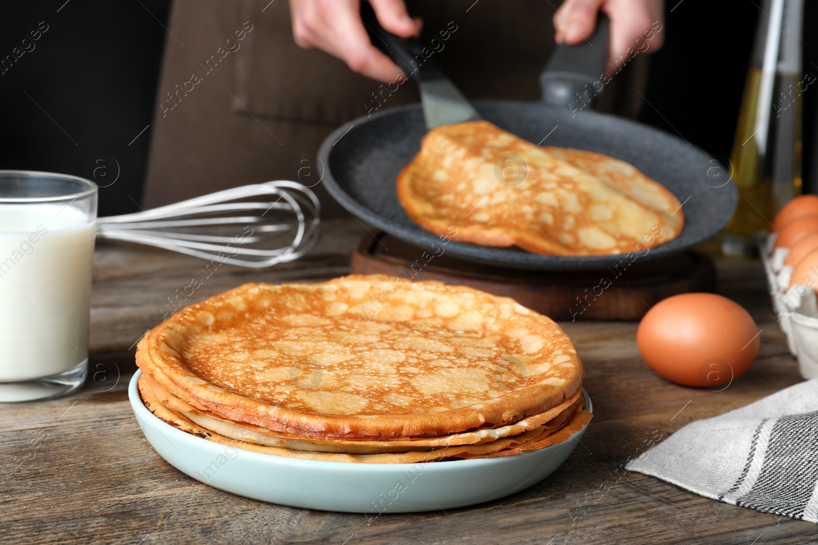 Photo of Woman cooking delicious thin pancakes at wooden table