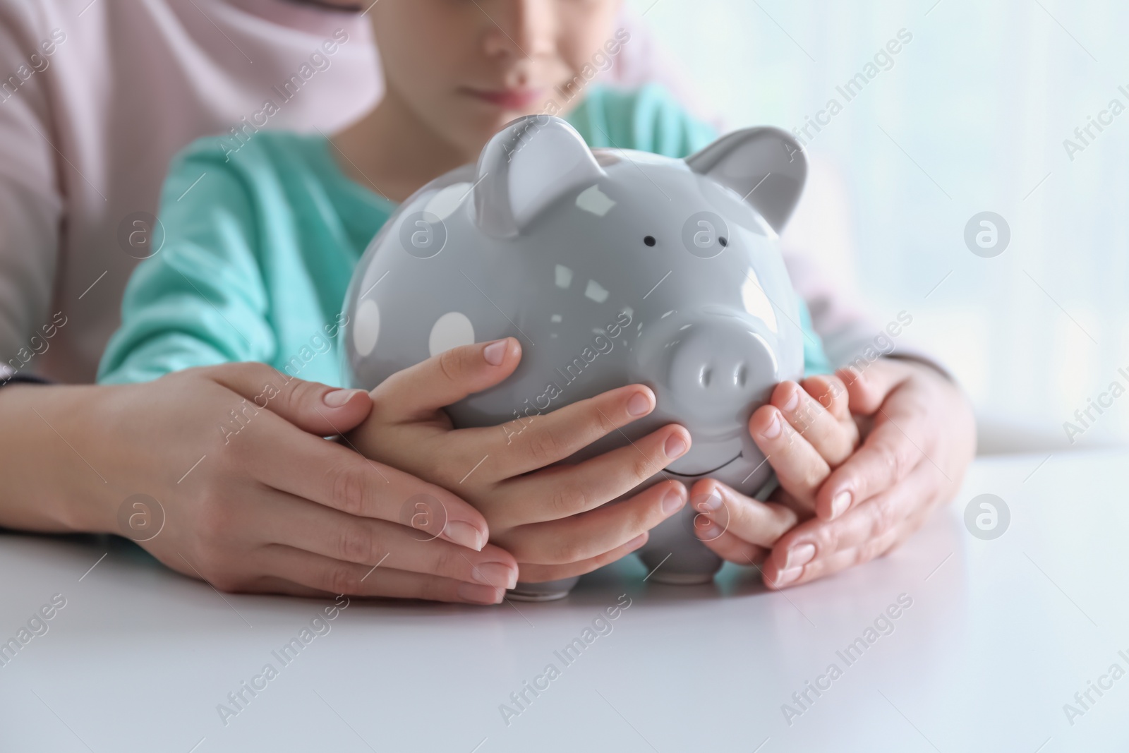 Photo of Mother and son with piggy bank at white table indoors, closeup