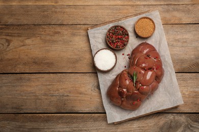 Fresh raw kidney meat with spices and rosemary on wooden table, top view. Space for text