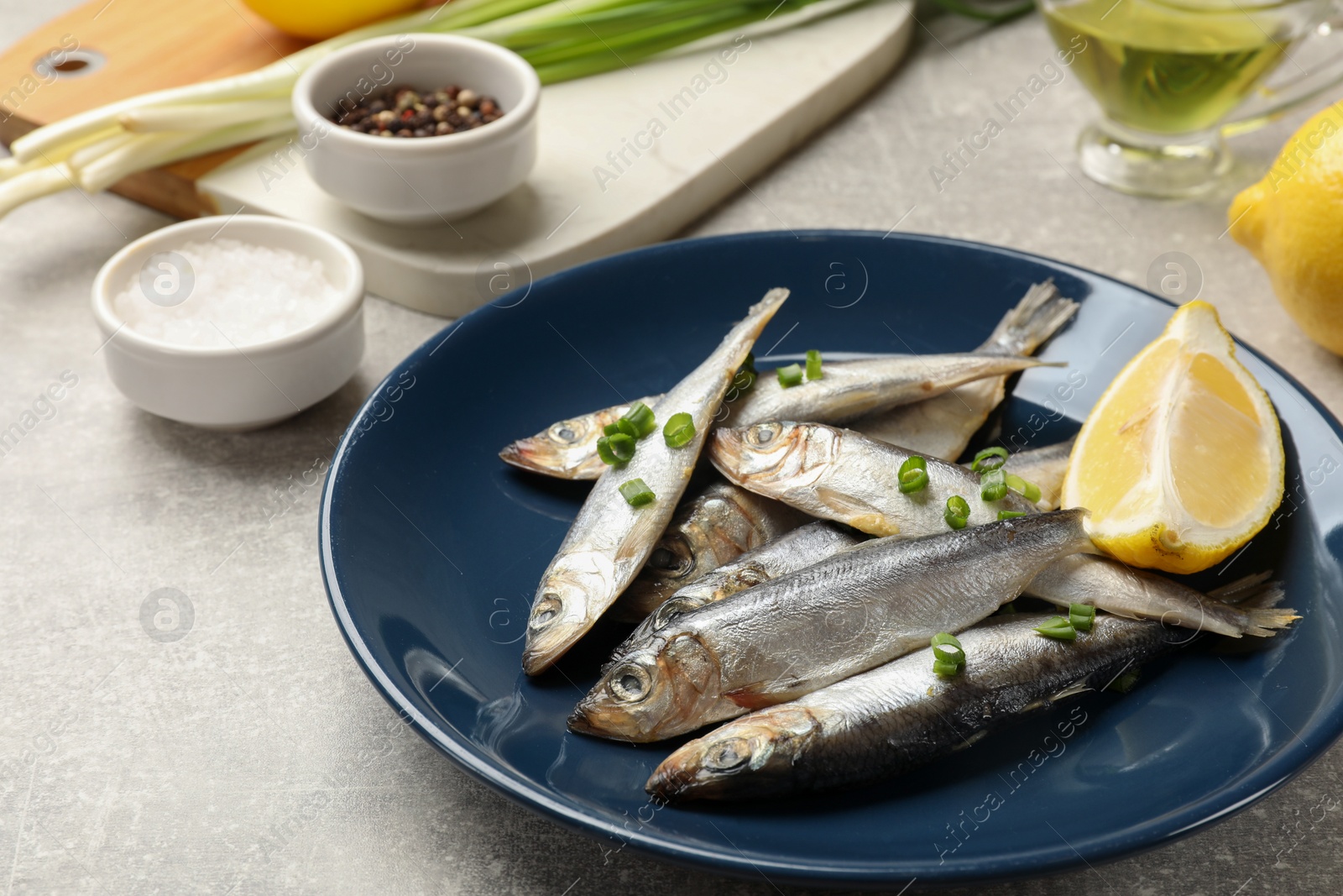 Photo of Fresh raw sprats, green onion, spices and cut lemon on grey table, closeup