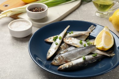 Photo of Fresh raw sprats, green onion, spices and cut lemon on grey table, closeup