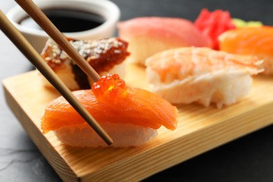 Taking delicious nigiri sushi with chopsticks from wooden board on black table, closeup
