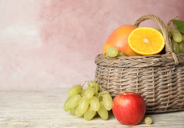 Photo of Wicker basket with different fruits on white wooden table near pink wall. Space for text