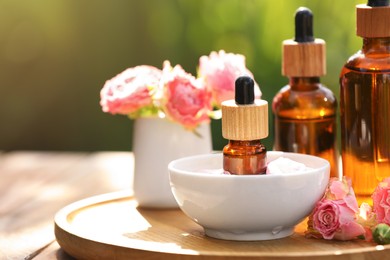 Photo of Bottles of rose essential oil and flowers on wooden table outdoors