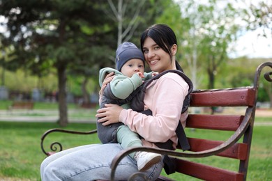 Mother holding her child in sling (baby carrier) on bench in park