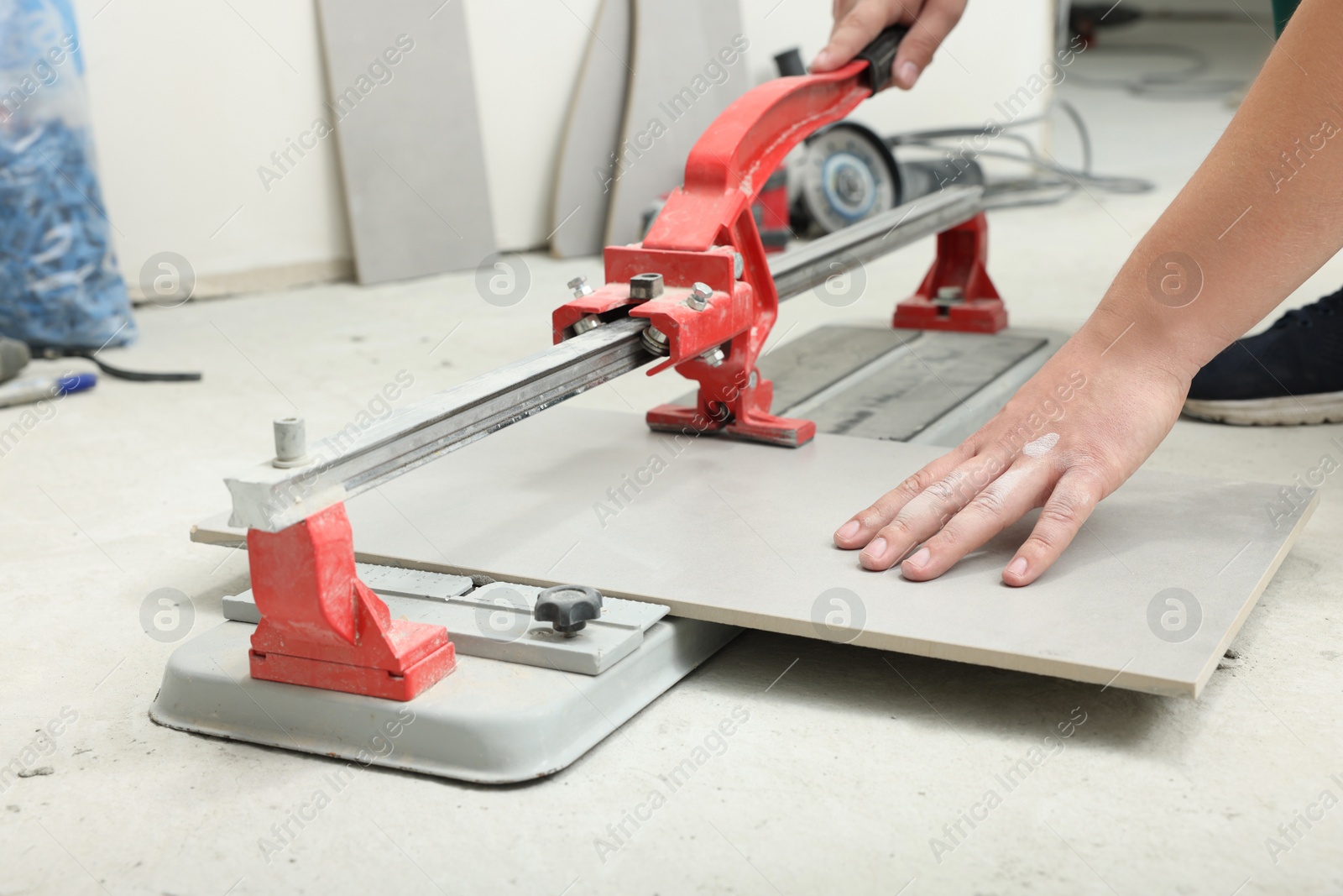 Photo of Worker using manual tile cutter indoors, closeup