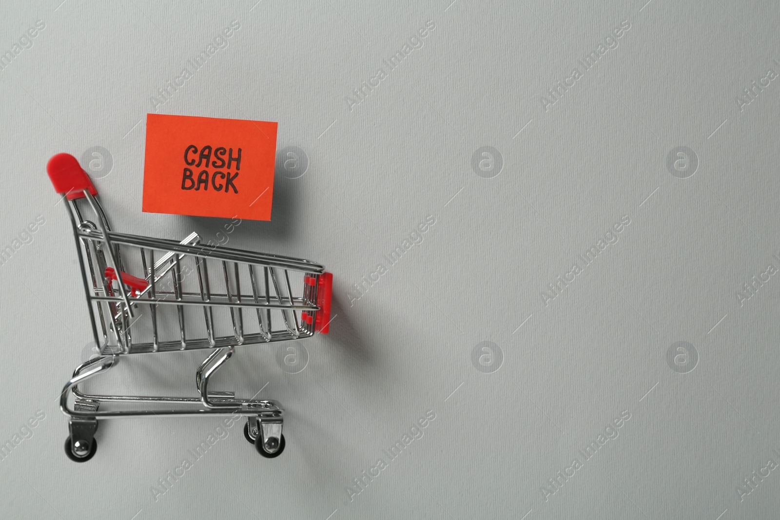 Photo of Card with word Cashback and shopping cart on light grey background, flat lay. Space for text