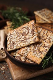 Cereal crackers with flax, sunflower, sesame seeds and rosemary on wooden table, closeup