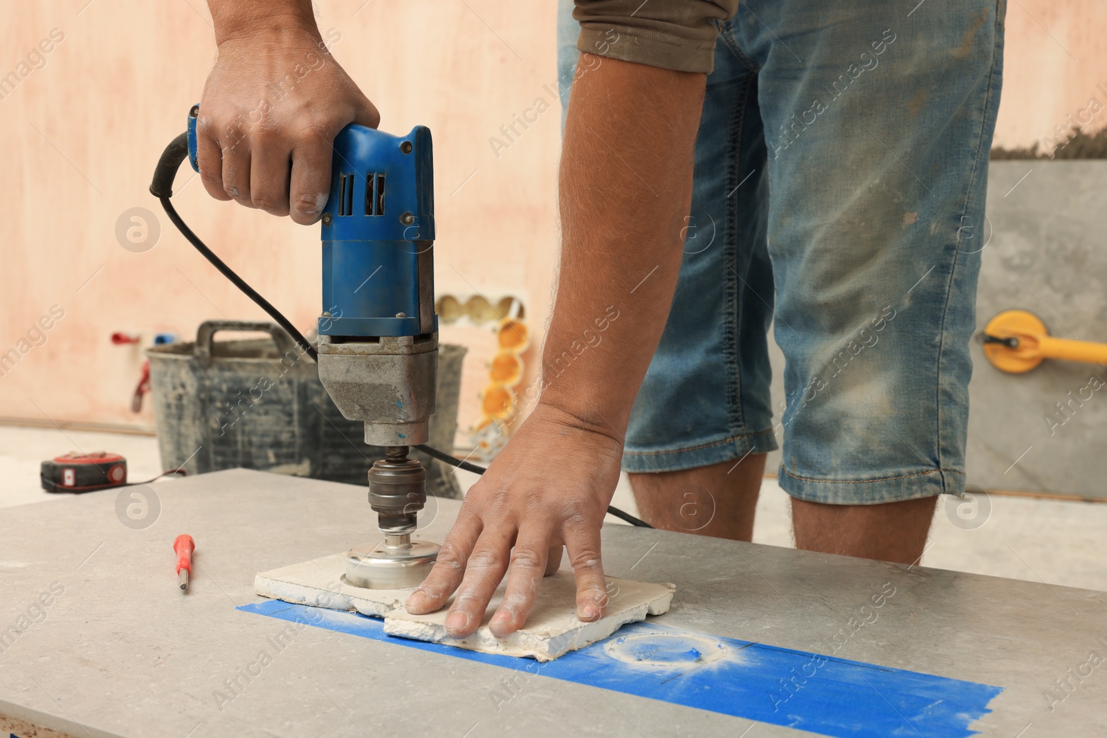 Photo of Worker making socket hole in tile indoors, closeup