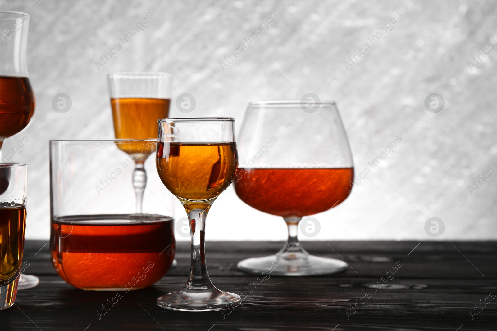 Photo of Different delicious liqueurs in glasses on dark wooden table