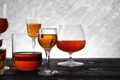 Photo of Different delicious liqueurs in glasses on dark wooden table