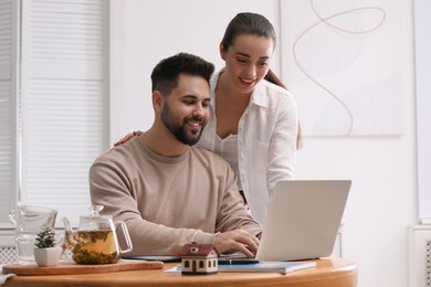 Happy young couple choosing new house using laptop at home. Mortgage concept