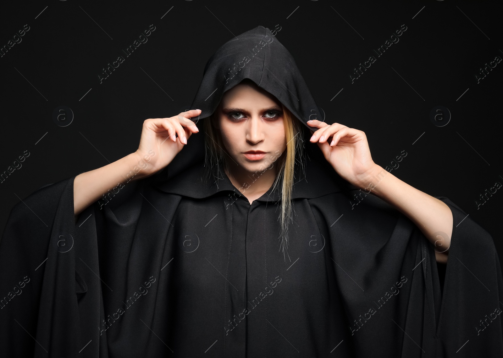 Photo of Witch in black mantle on dark background. Scary fantasy character