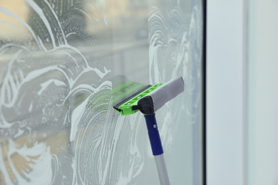 Cleaning window with squeegee indoors. Household chores