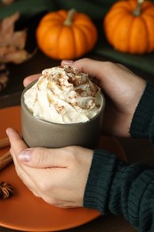 Woman holding cup of tasty pumpkin spice latte with whipped cream at table, closeup