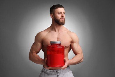 Photo of Young man with muscular body holding jar of protein powder on grey background