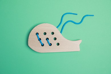 Photo of Wooden whale figure with holes and lace on green background, top view. Educational toy for motor skills development