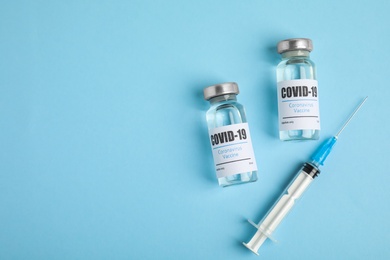 Photo of Vials with coronavirus vaccine and syringe on light blue background, flat lay. Space for text