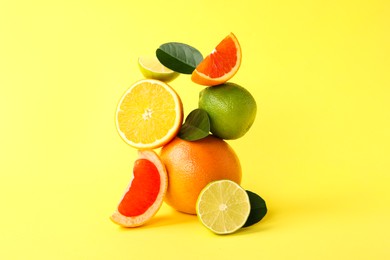 Fresh ripe citrus fruits and green leaves on yellow background