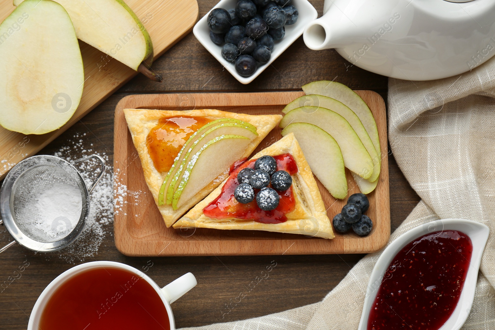 Photo of Fresh tasty puff pastry with jam, blueberries and pear served on wooden table, flat lay