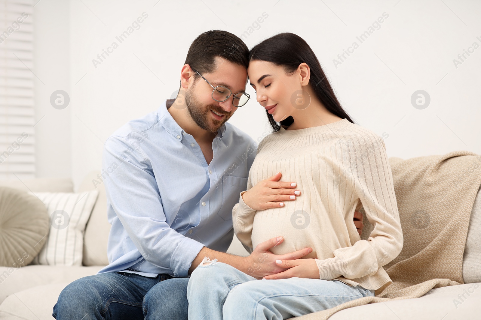 Photo of Pregnant woman with her husband on sofa at home