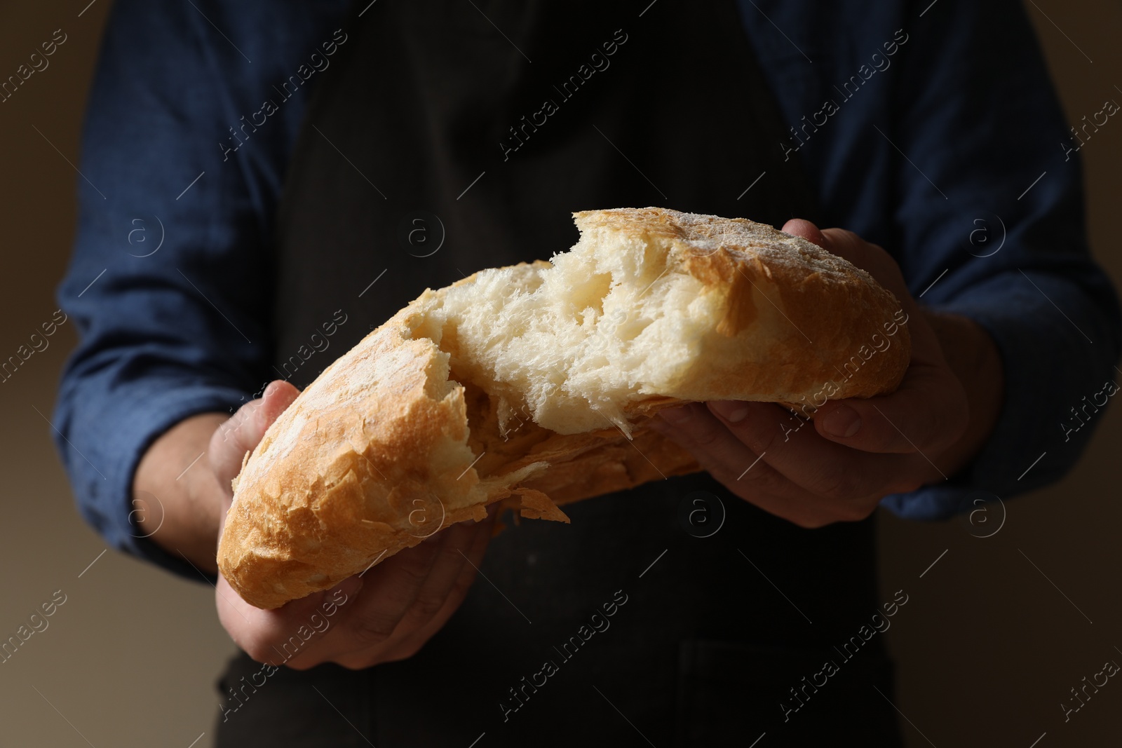 Photo of Man breaking loaf of fresh bread on dark background, closeup