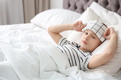 Photo of Little boy suffering from headache while lying in bed at home