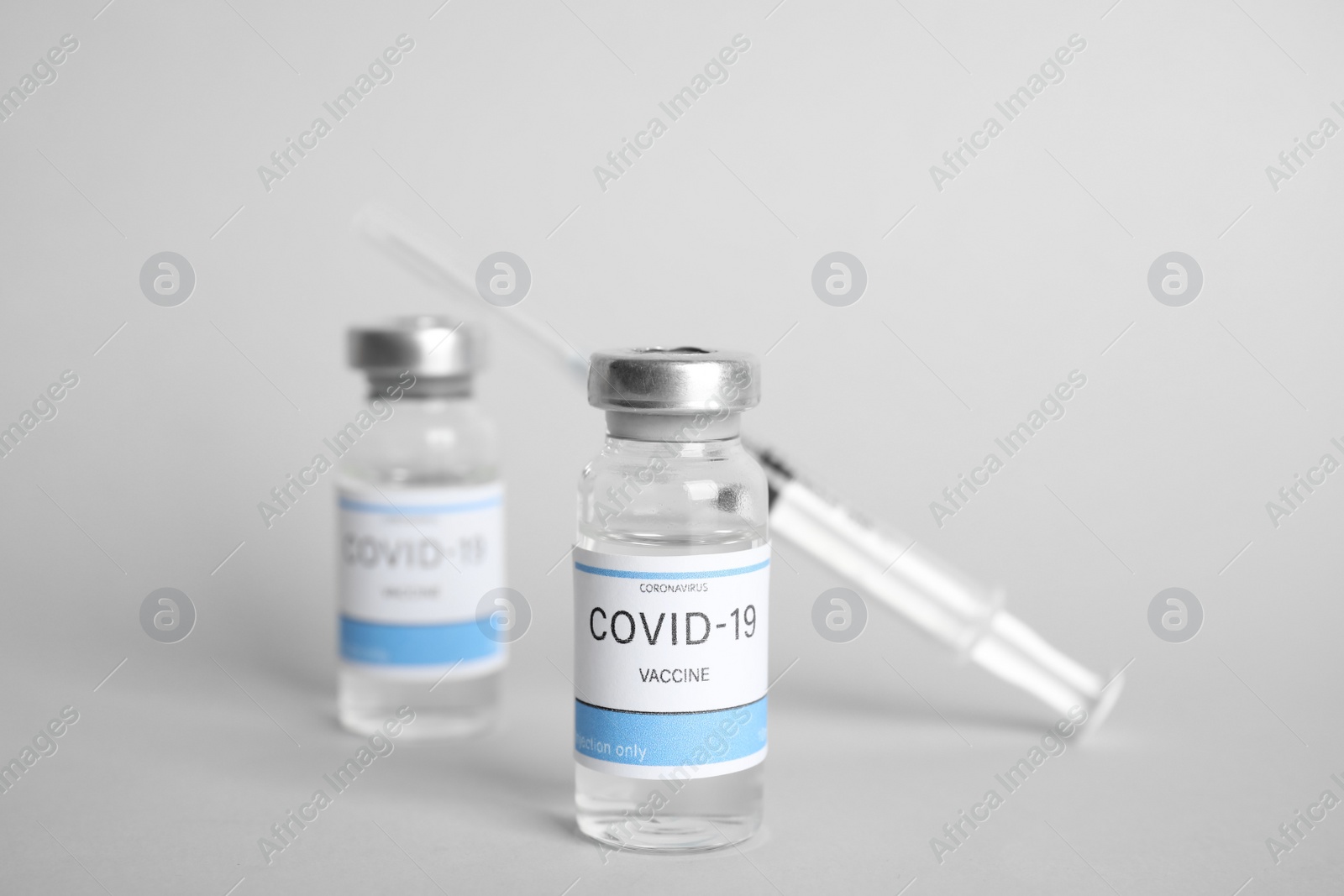 Photo of Vials with coronavirus vaccine and syringe on light background