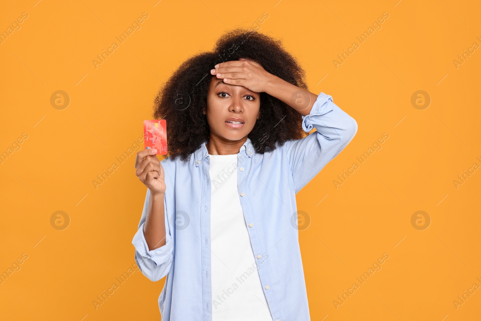 Photo of Confused woman with credit card on orange background. Debt problem