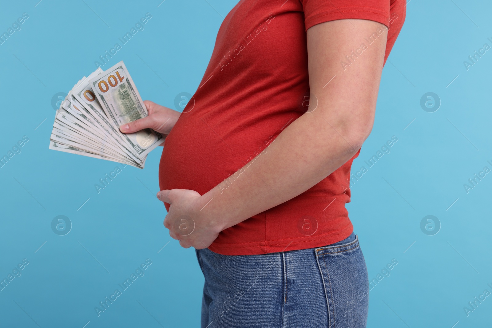 Photo of Surrogate mother. Pregnant woman with dollar banknotes on light blue background, closeup