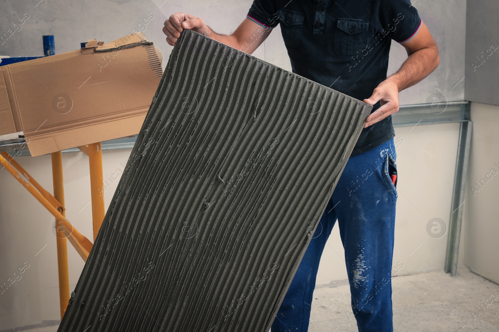 Photo of Worker holding tile with adhesive mix indoors, closeup